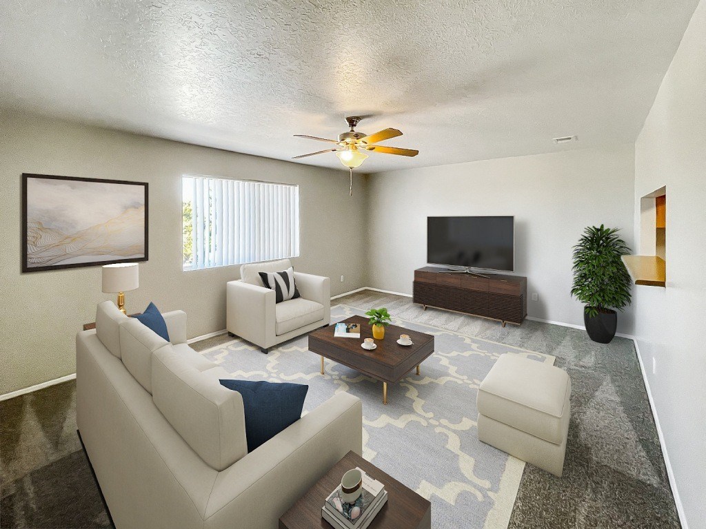 A living room with a white couch, a coffee table, a flat screen TV, and a ceiling fan.